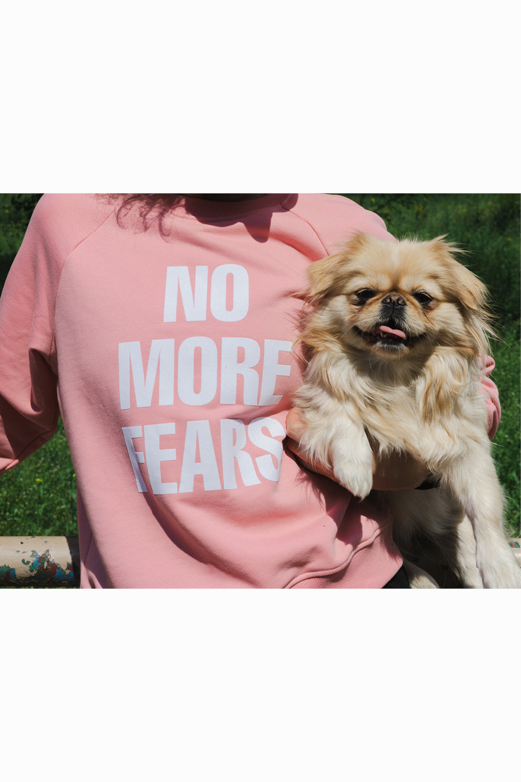 Różowy sweter z napisem NO MORE FEARS, kobieta trzyma psa na zewnątrz