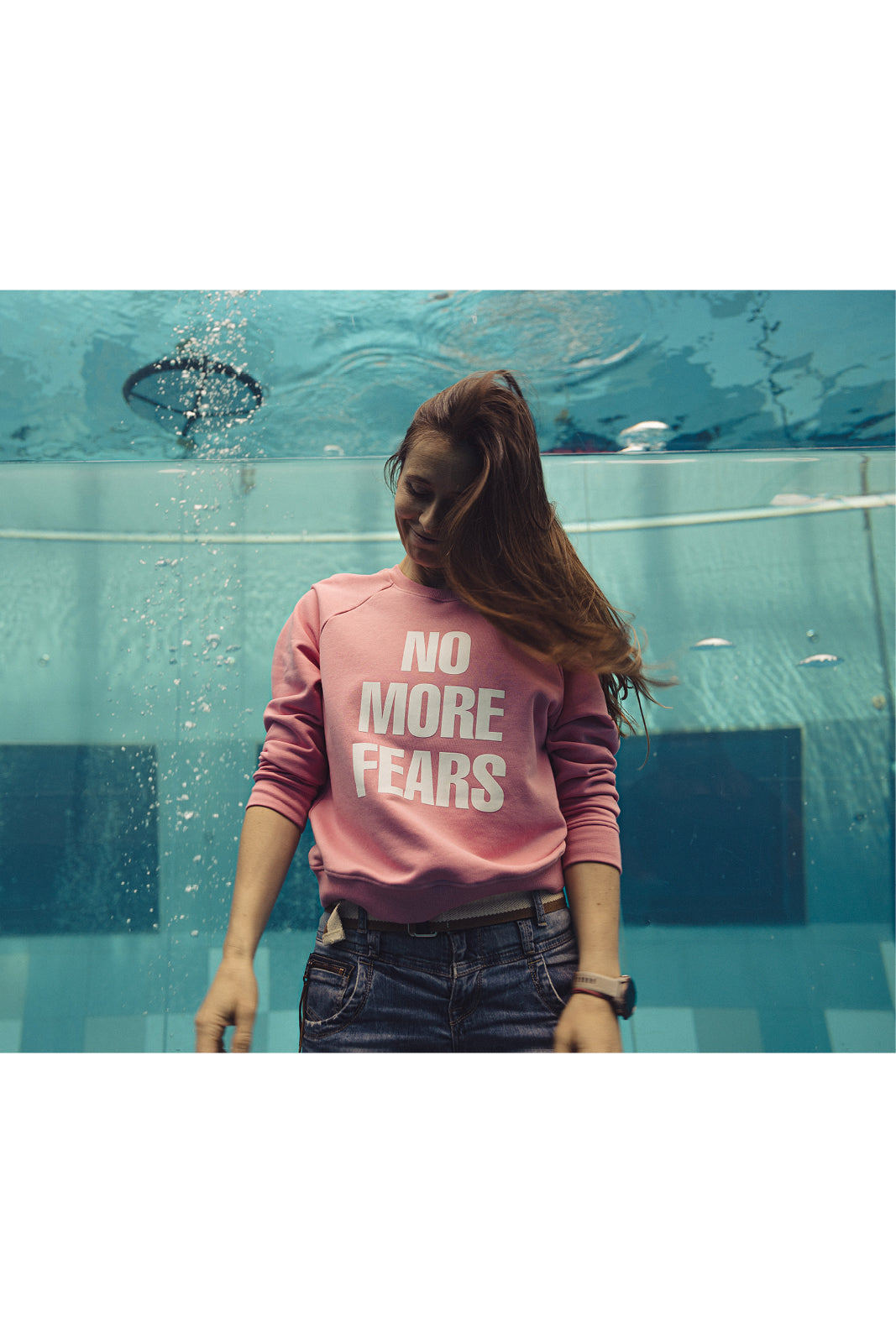 Różowy sweter z napisem NO MORE FEARS, modna stylizacja z jeansami, kobieta w basenie