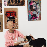 Mężczyzna w różowej bluzie z napisem 'NO MORE' głaszcze psa na tle sztuki ulicznej z napisami 'GAY ANGER' i 'SMASH FASCISM'
