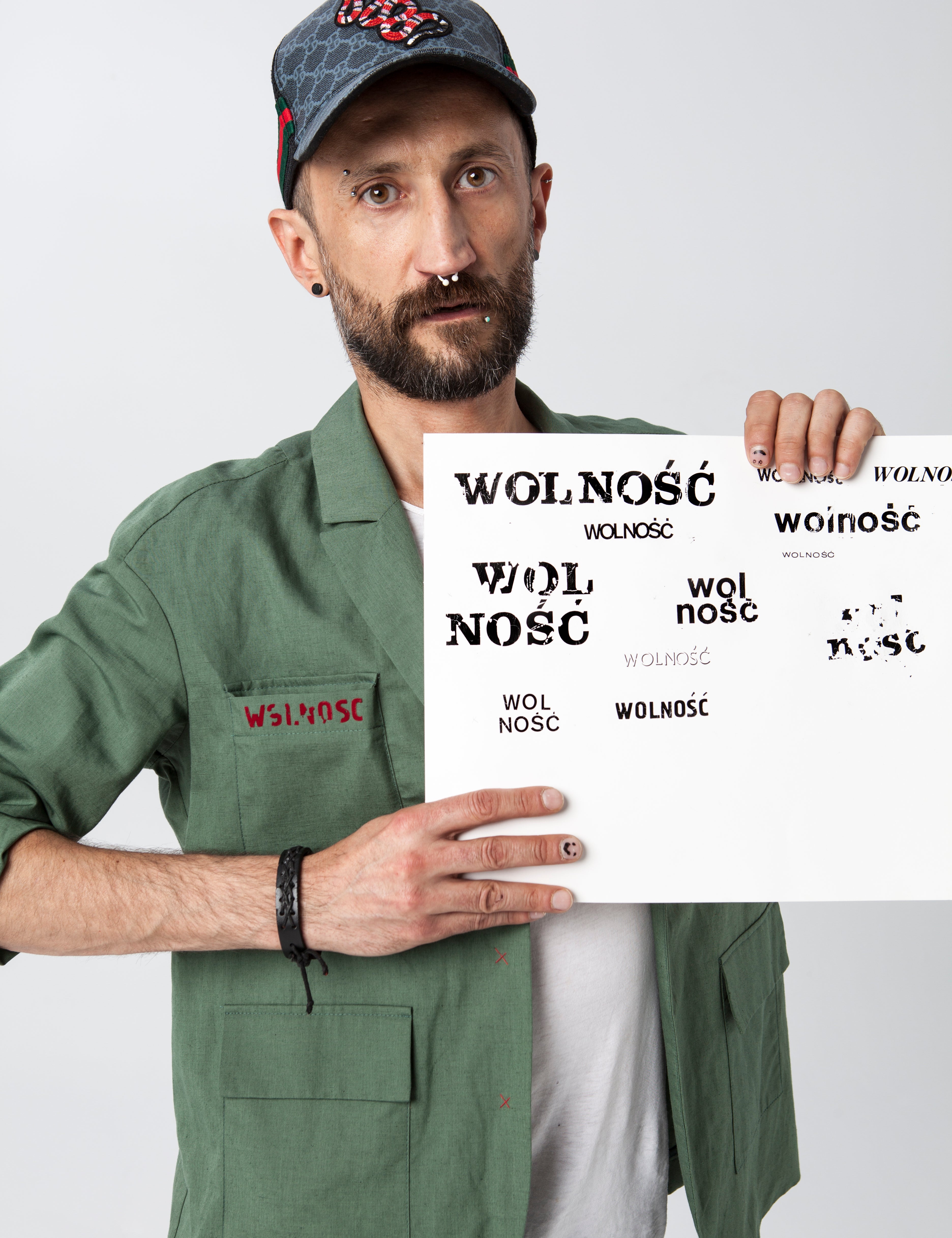 Mężczyzna w zielonej koszuli i czapce trzyma plakat z napisem 'WOLNOŚĆ'. Moda z kulturą i wygodą, polskie wykonanie.