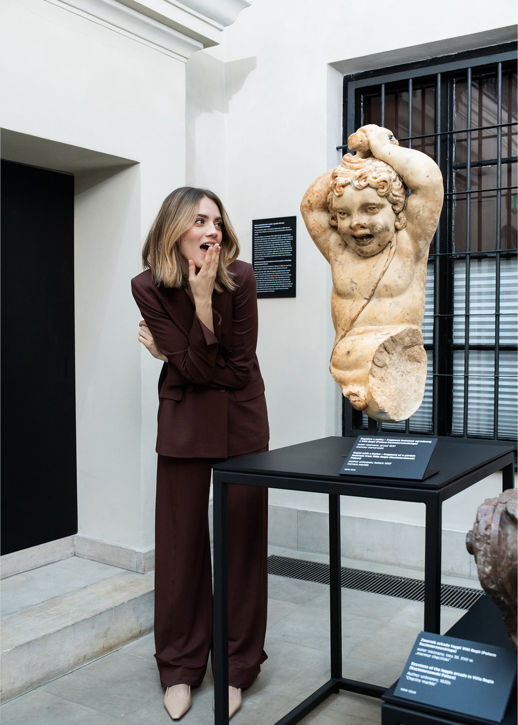 Kobieta w brązowym garniturze przy rzeźbie w muzeum, stylowa moda z kulturą i sztuką
