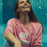 Kobieta w różowej bluzie z napisem NO MORE TEARS, uśmiechnięta przy basenie – moda z kulturą i komfortem