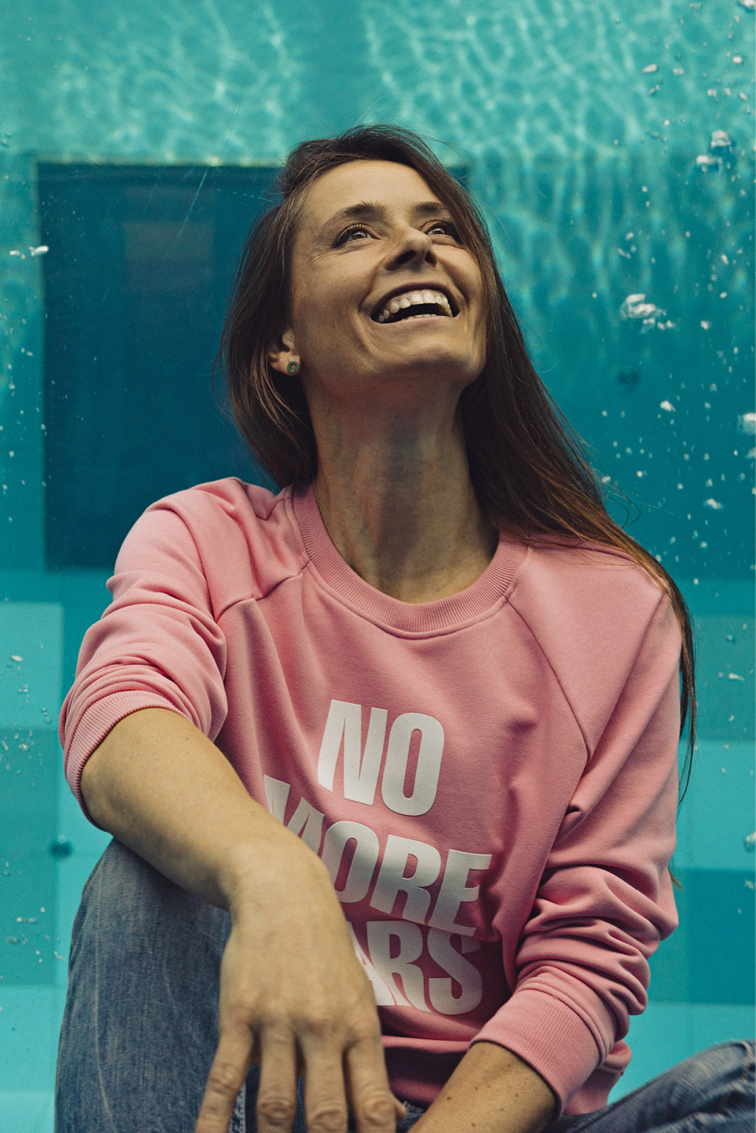 Kobieta w różowej bluzie z napisem NO MORE TEARS, uśmiechnięta przy basenie – moda z kulturą i komfortem