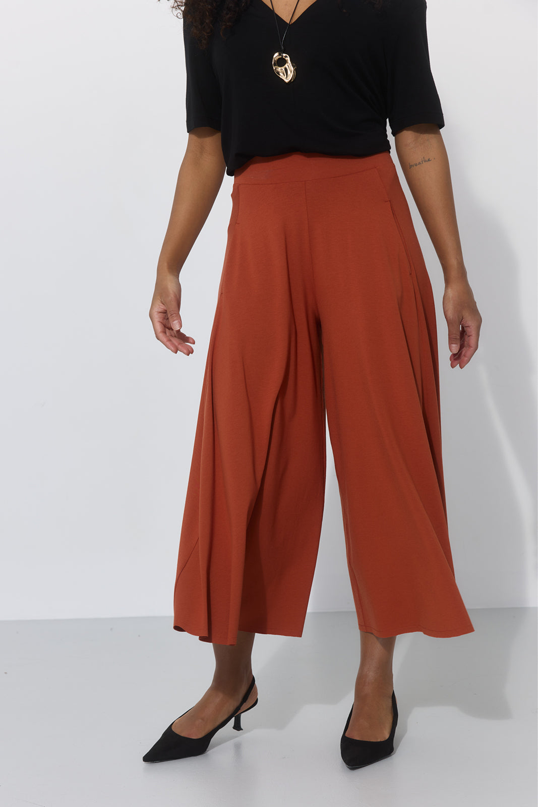 Szerokie spodnie culottes w kolorze ceglastym, idealne na co dzień, z czarną bluzką i obcasami
