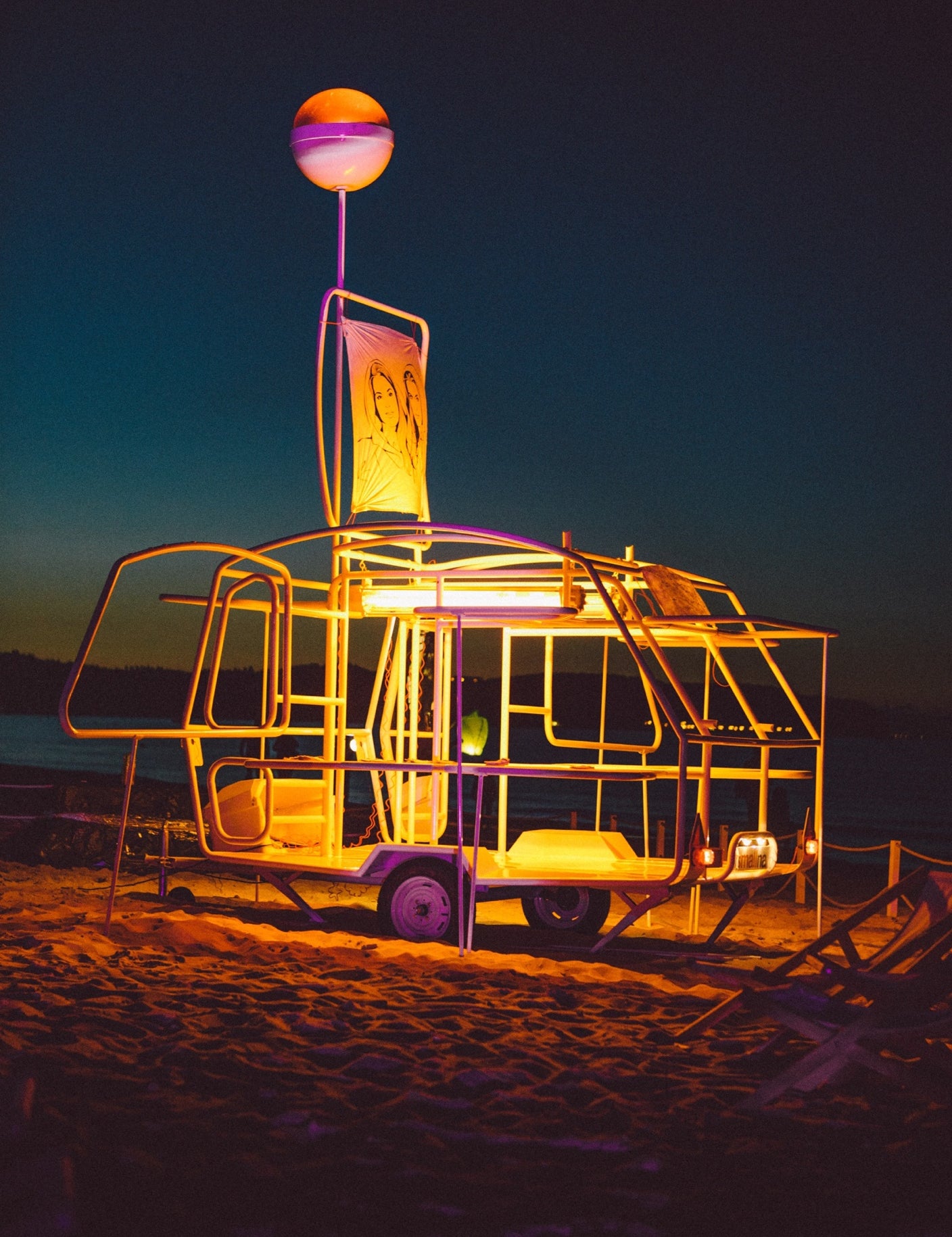Świecąca konstrukcja na plaży nocą z neonowymi światłami i grafiką, idealna dla stylowej sesji zdjęciowej.