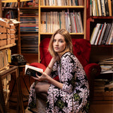 Kobieta w kwiecistej sukience siedzi na czerwonym fotelu z książką w bibliotece